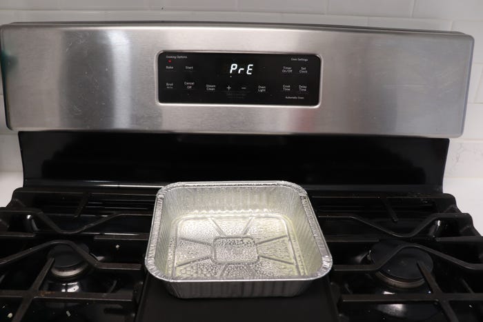 An oven preheats with a foil pan on the stove.