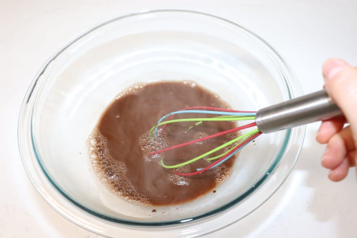 A whisk mixes cocoa powder and water.